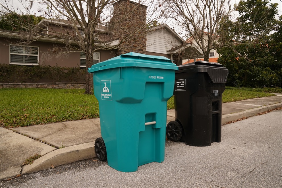 Teal and black trash cans placed in front of a house.